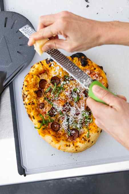 ATK Reviews member grating Parmesan over finished pepperoni pizza.